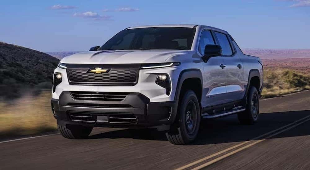 A white 2024 Chevy Silverado EV is shown driving on a highway.