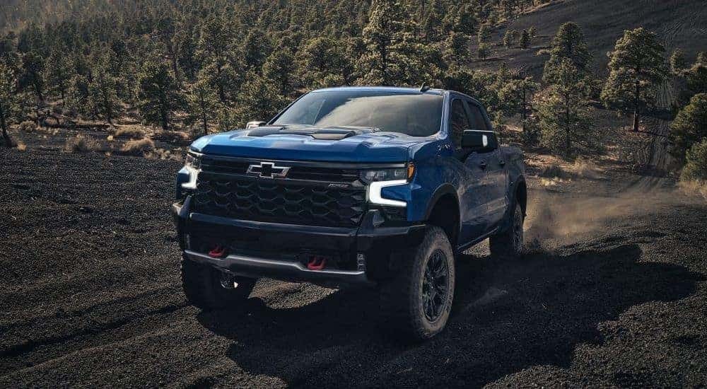 A blue 2024 Chevy Silverado 1500 ZR2 is shown driving on a dirt road.