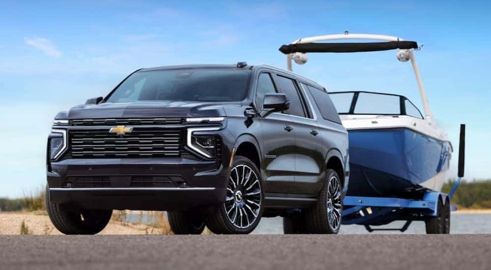 A blue 2025 Chevy Suburban for sale is shown towing a boat.