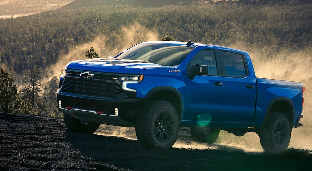 Blue 2026 Chevy Silverado 1500 driving off-road up a hill.