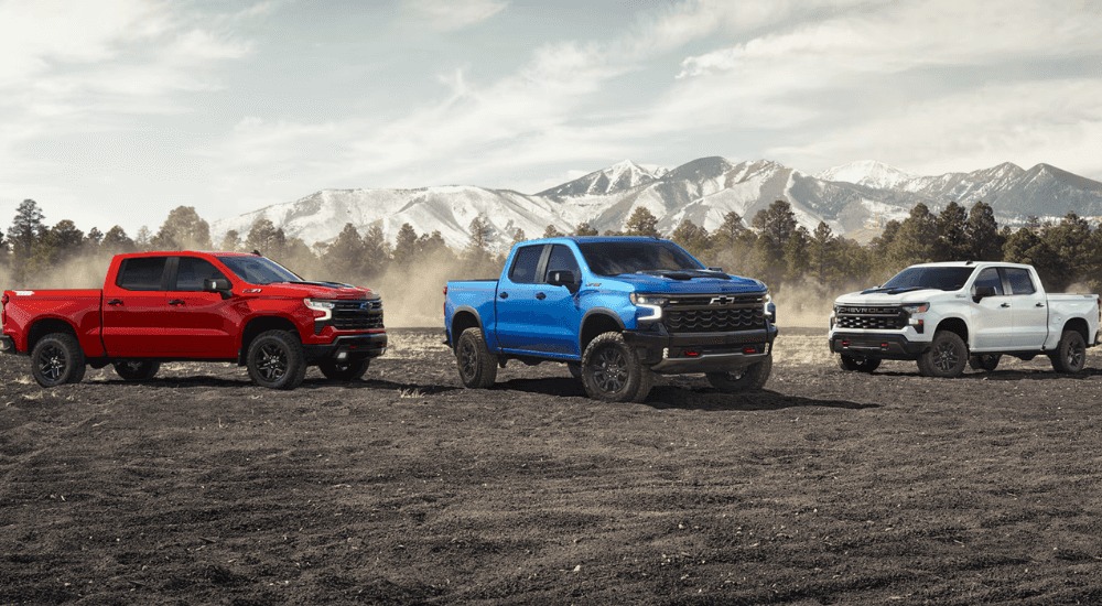 Three 2026 Chevy Silverado 1500's in red, white, and blue parked on dirt.
