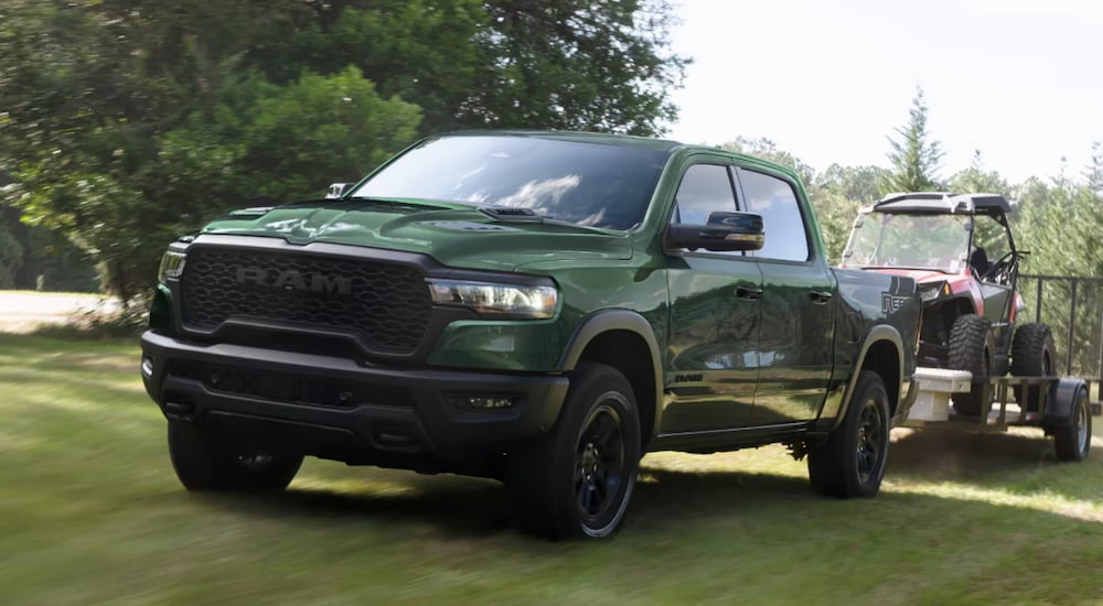 Green 2026 Ram 1500 towing an ATV near a forest.