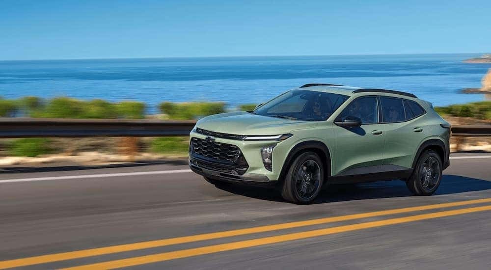 A green 2024 Chevy Trax is driving on a winding highway near a lake.