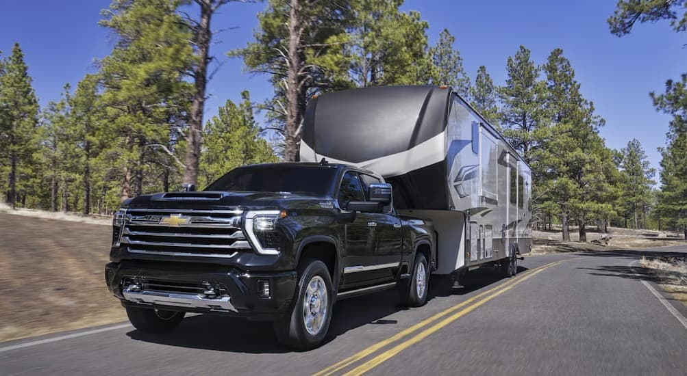 A black 2026 Chevy Silverado towing a trailer to view heavy duty trucks for sale.