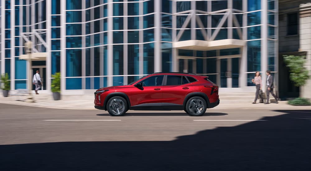 Side of a red 2026 Chevy Trax RS driving down a city street.