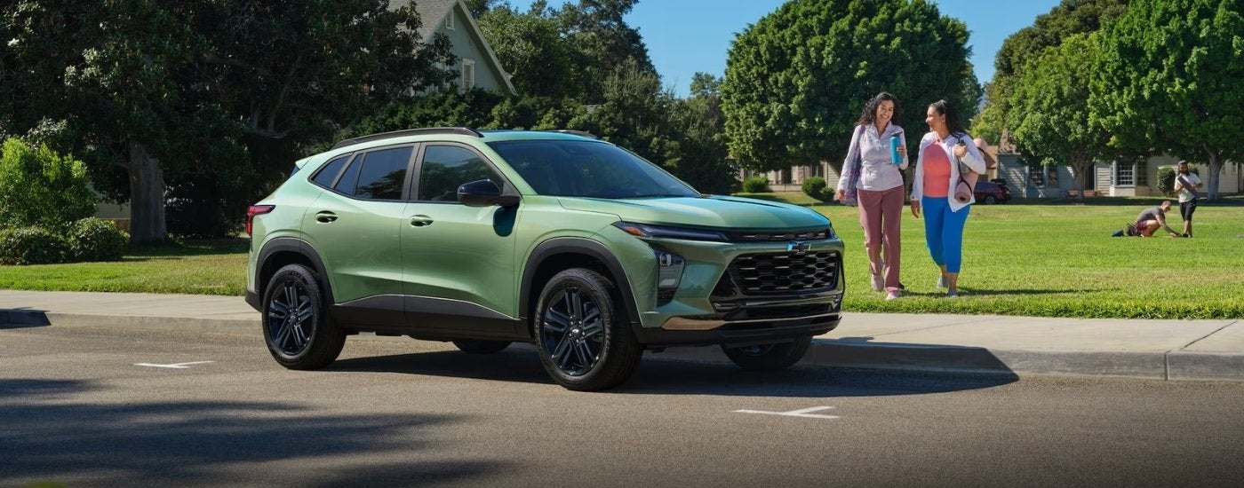 A green 2026 Chevy Trax ACTIV parked by a field and two people.