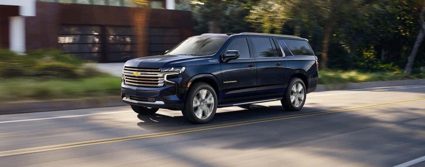 A blue 2024 Chevy Suburban High Country is shown driving to view a Chevy Suburban for sale