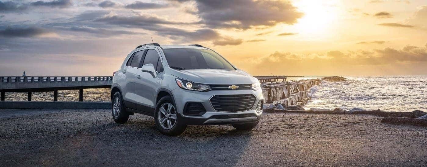 A close up shows the badge on a silver 2021 Chevy Trax parked by a jetty