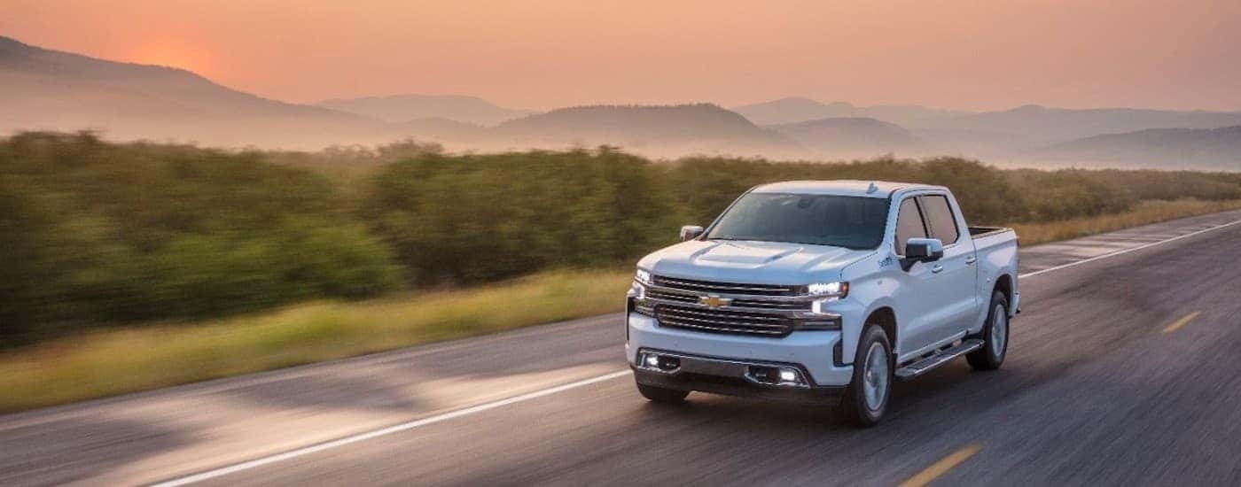 A white 2021 Chevy Silverado 1500 High Country is shown driving on a wet road at dusk.