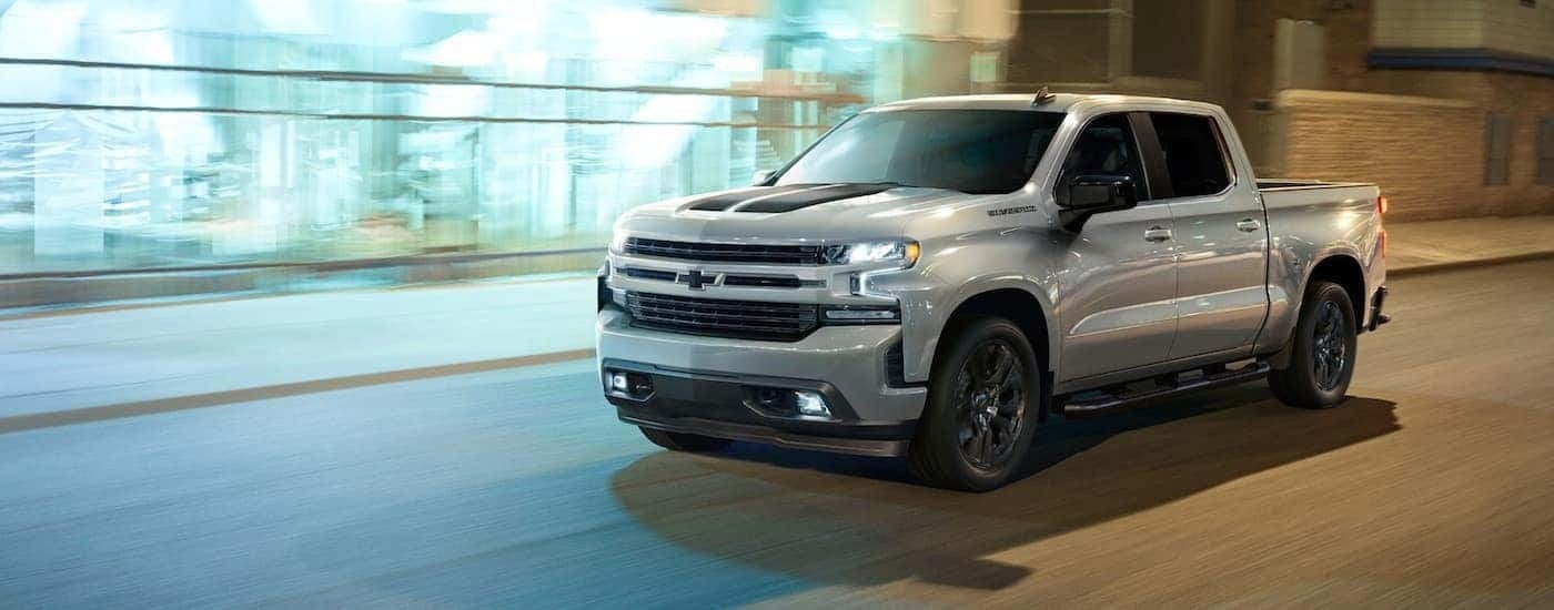 A white 2023 Chevy Silverado 1500 RST Rally is shown driving on a city street.