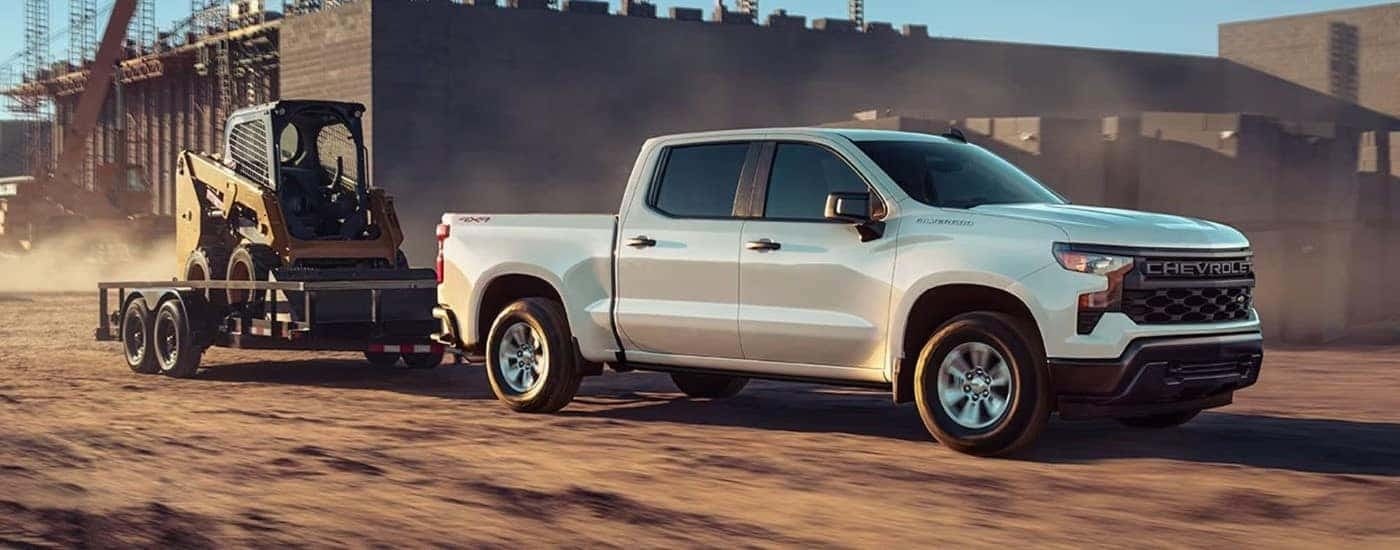 A black 2023 Chevy Silverado 1500 High Country is shown towing a bobcat