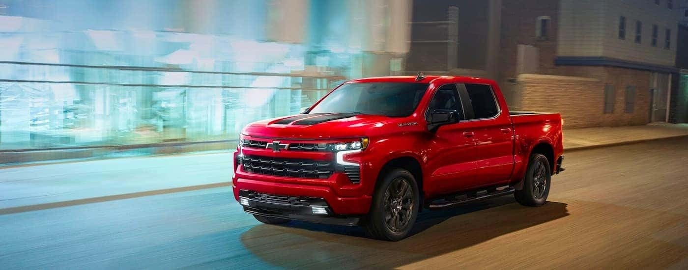 A red 2024 Chevy Silverado 1500 RST is shown driving on a city street at night.