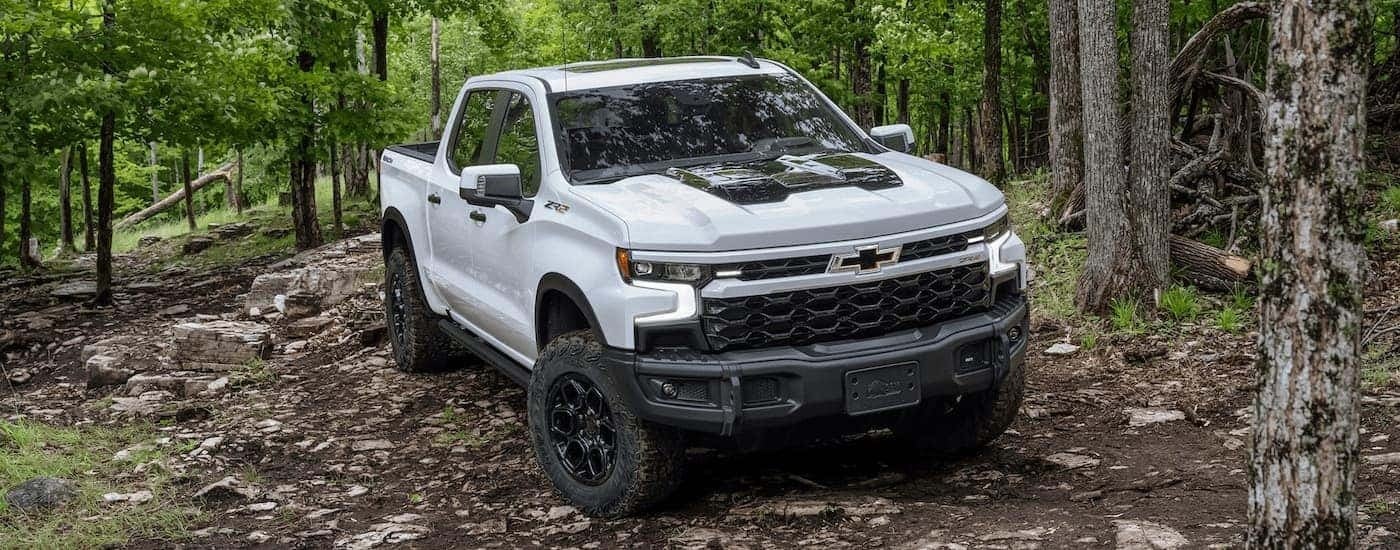 A white 2024 Chevy Silverado 1500 ZR2 is driving on a rocky forest trail.