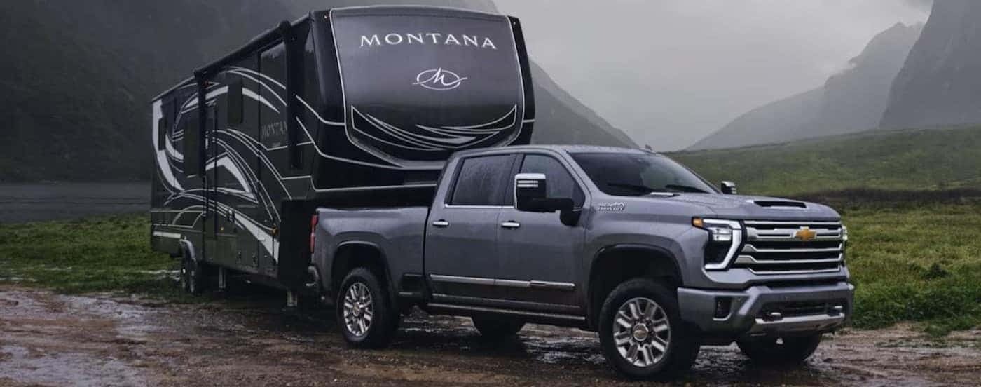 A gray 2024 Chevy Silverado 2500 HD High Country is shown towing a trailer.