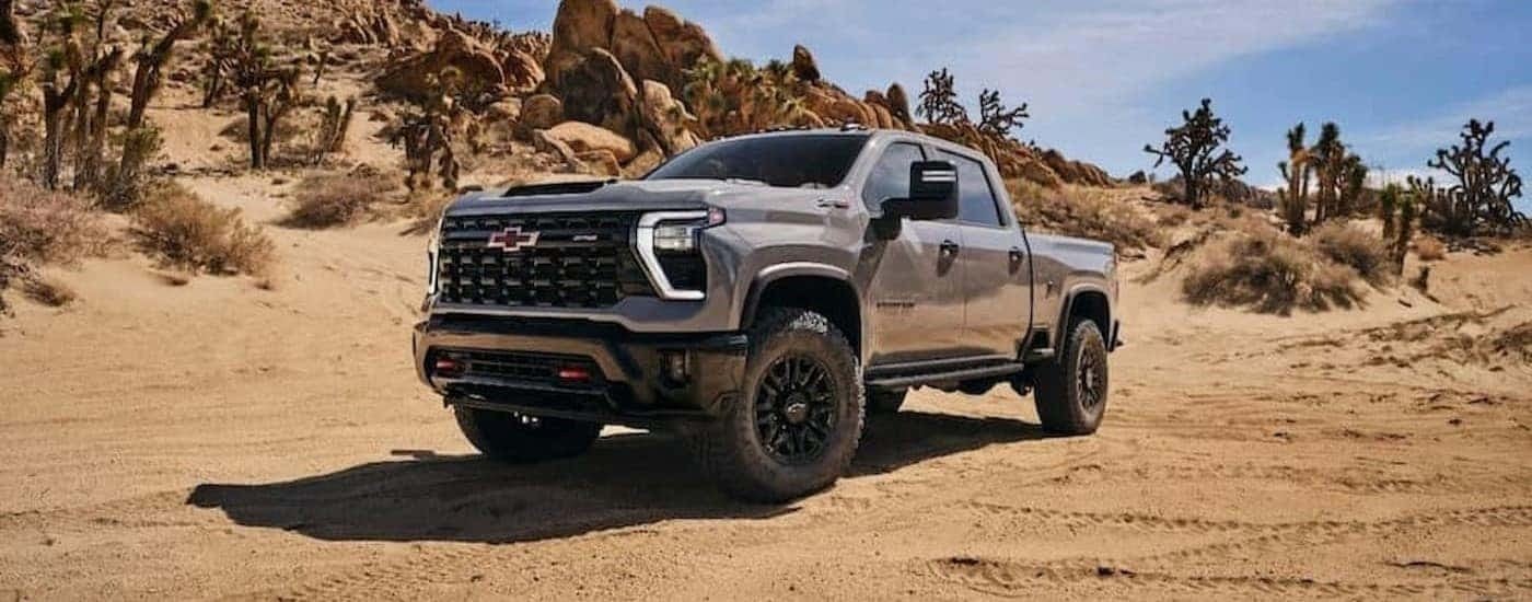 A silver 2024 Chevy Silverado 2500 ZR2 is shown parked on sand.